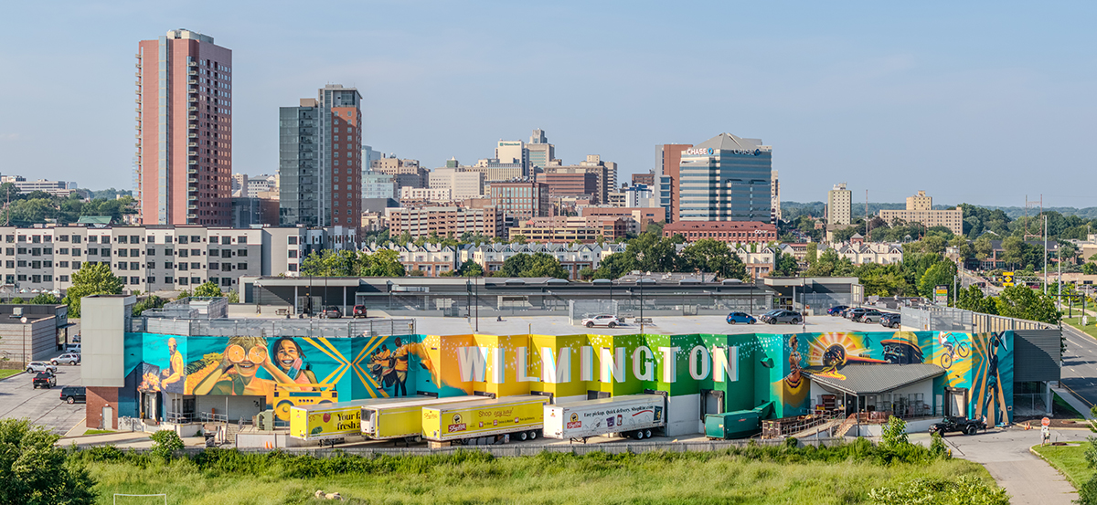 Wide-angle aerial view of the ShopRite mural at Christina Crossing in Wilmington, Delaware, painted by Christian Kanienberg (WISH), featuring vibrant scenes of community life, music, sports, and food culture.