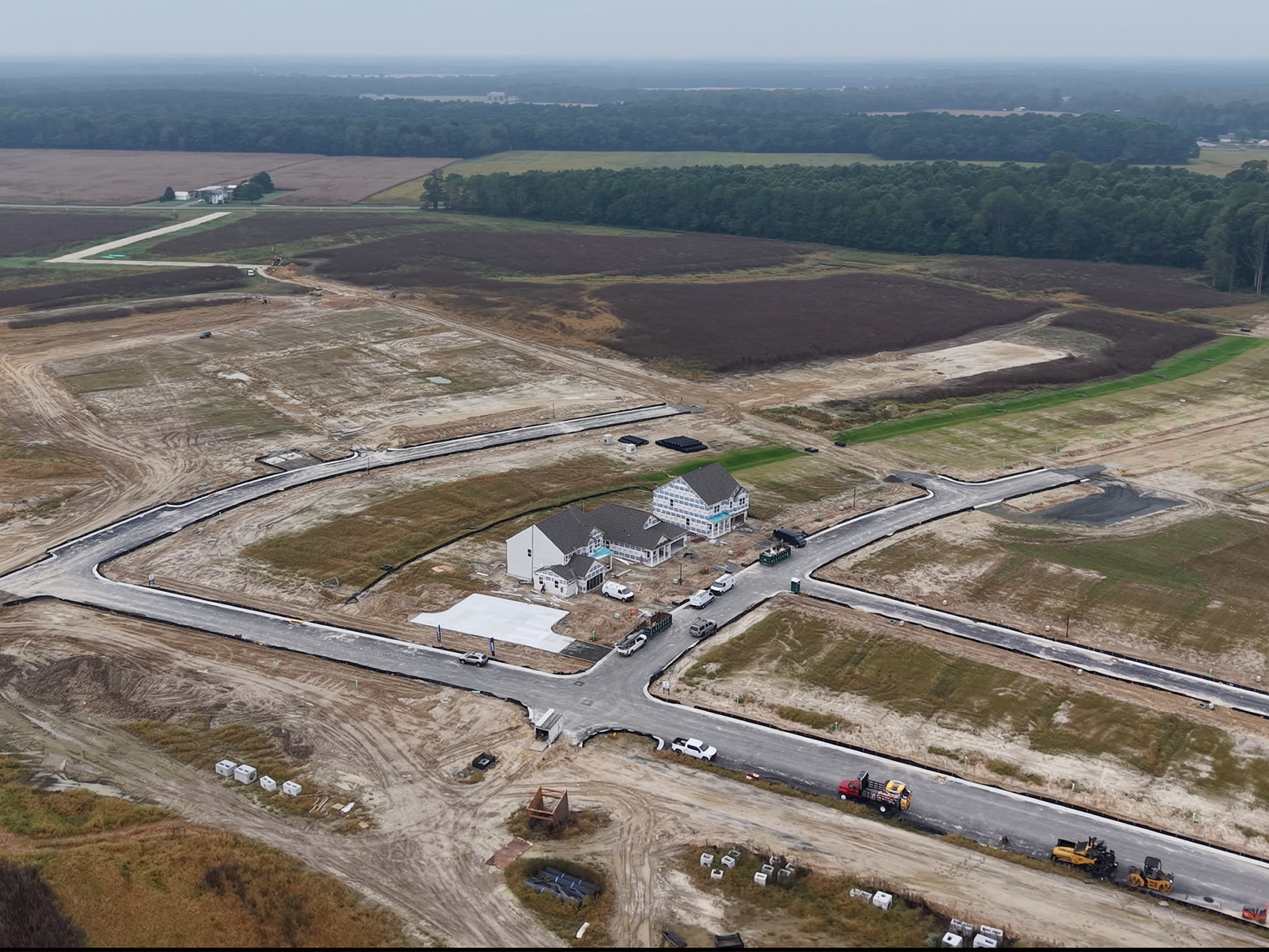Wide aerial view showing construction site within surrounding land and development