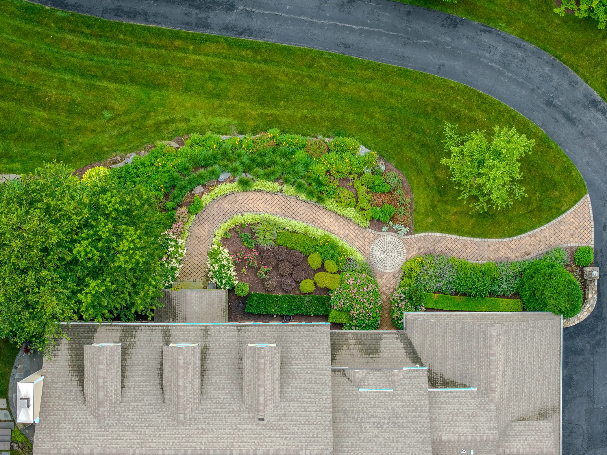Straight-down aerial view of Kennett Square residence showing curved brick paver entry path with circular medallion detail, layered perennial planting beds, and full design-build layout by Eastern Horticultural Services