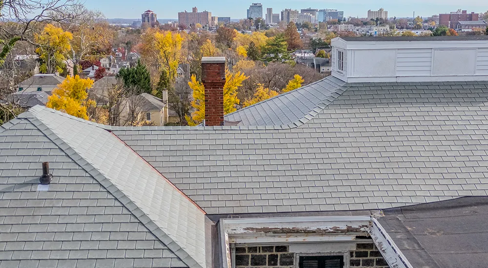 Aerial roof inspection showing chimney, gutter line, and fascia damage with city skyline in background